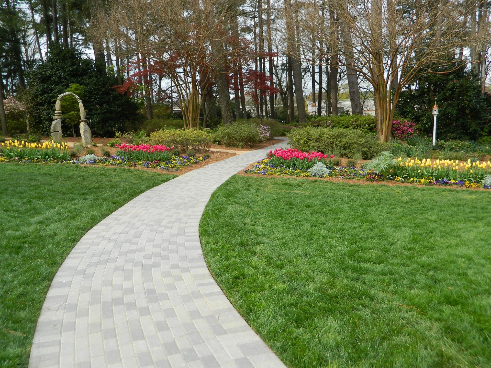 Paver path through a maintained garden with tulip beds and clipped lawn in Raleigh